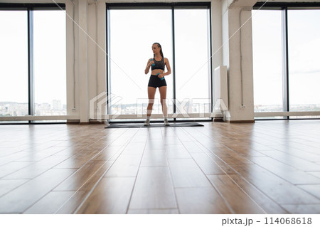 Fit young woman wearing workout gear stands on mat. 114068618