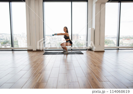 Young woman exercising with dumbbells in a bright gym 114068619