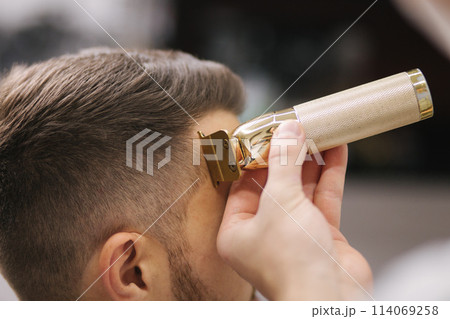 Professional hairdresser uses a hair clipper for fringing hair for a handsome barber man Professional hairdresser uses a hair clipper for fringing hair for a handsome barber man 114069258