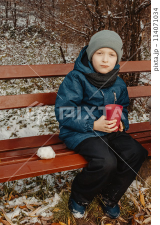 Winter Picnic Delight: 8-Year-Old Boy Savoring Tea on Snowy Bench in Rural Park. an 8-year-old boy enjoying a delightful moment on a snow-covered bench in a tranquil rural park. Winter Picnic Delight: 8-Year-Old Boy Savoring Tea on Snowy Bench in Rural Park. an 8-year-old boy enjoying a delightful moment on a snow-covered bench in a tranquil rural park. 114071034