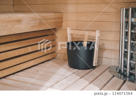 A wooden bench with a black bucket on it. The bucket is filled with water and a wooden stick.  114071564