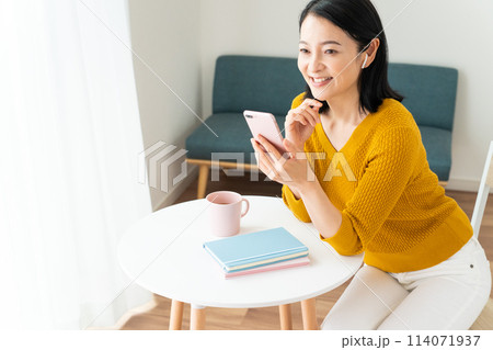 イヤホンをしてスマホを見るミドル女性 114071937
