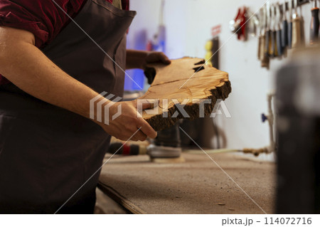 Carpenter holding timber block, doing quality assurance on it before starting furniture assembling in workshop, close up shot. Manufacturer in joinery preparing piece of wood for carving Carpenter holding timber block, doing quality assurance on it before starting furniture assembling in workshop, close up shot. Manufacturer in joinery preparing piece of wood for carving 114072716