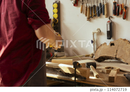 Woodworking specialist using manual sandpaper to sander lumber block, making furniture in assembling shop during job shift. Handyman polishing surface of piece of wood with abrasive material Woodworking specialist using manual sandpaper to sander lumber block, making furniture in assembling shop during job shift. Handyman polishing surface of piece of wood with abrasive material 114072719