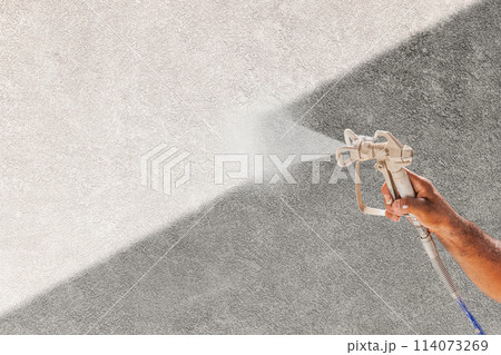 Professional Spray Painter Holding Spray Gun Spraying White Paint Over Grey Stucco Surface. 114073269
