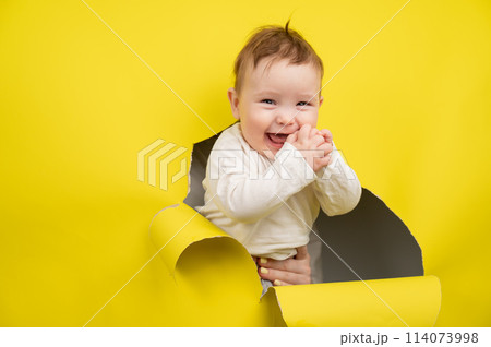 Cheerful baby rips and sticks out through yellow cardboard background. Cheerful baby rips and sticks out through yellow cardboard background. 114073998