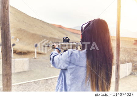 Woman empowered shooter aiming assault rifle at target. Selective Focus Woman empowered shooter aiming assault rifle at target. Selective Focus 114074027