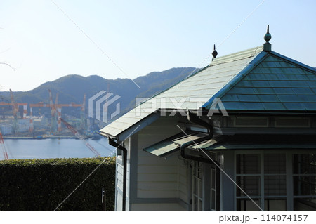 旧長崎高商表門衛所の屋根越しに長崎の海と三菱重工業長崎造船所を眺める（日本 長崎県長崎市） 114074157