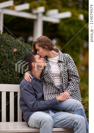Autumn Romance: Young Couple Embracing and Kissing on Park Bench. Young couple kissing and rejoices at the lake. lovely young couple kissing outdoors in autumn. Embraced in Autumn's Warmth: Couple's Autumn Romance: Young Couple Embracing and Kissing on Park Bench. Young couple kissing and rejoices at the lake. lovely young couple kissing outdoors in autumn. Embraced in Autumn's Warmth: Couple's 114074974
