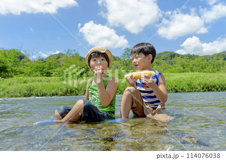 夏の川原で夏野菜を持つ男の子たち 114076038