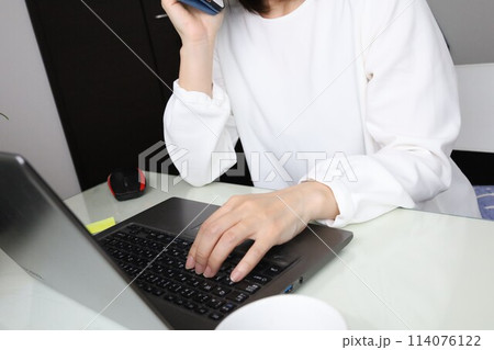 パソコン前で電話をする女性 114076122