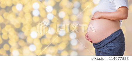 pregnant woman holding her pregnant belly over holiday bokeh lights background 114077828