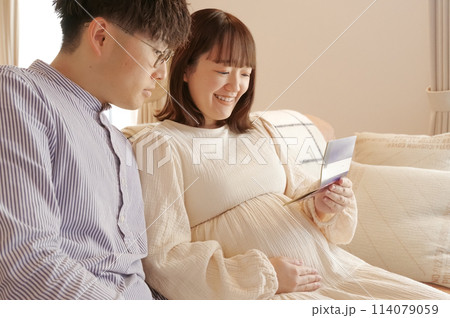 通帳を見ながら話し合いをする妊婦と男性 114079059