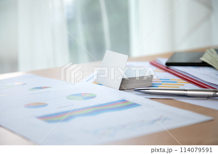 Enhancing strategic planning, workspace includes business reports, colorful pie charts, and graphs, along with tools such as notepad, pen, and tablet for efficient decision-making 114079591