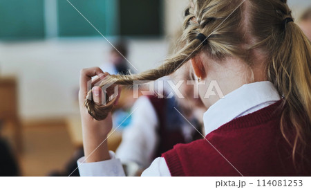 A girl touches a ponytail of her hair during class. A girl touches a ponytail of her hair during class. 114081253