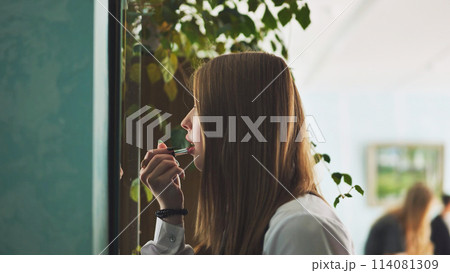 A schoolgirl paints her lips in front of the mirror. 114081309