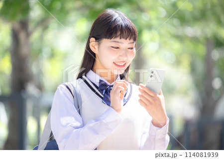 イヤホンを付けてスマホを見ている女子高校生 114081939