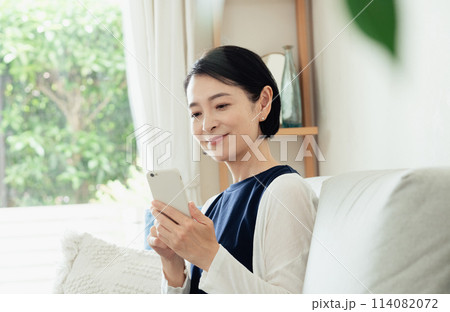 リビングでスマートフォンを操作する主婦 リビングでスマートフォンを操作する主婦 114082072