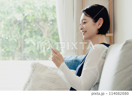 リビングでスマートフォンを操作する主婦 114082080