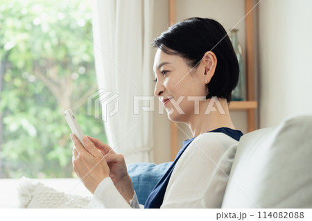 リビングでスマートフォンを操作する主婦 リビングでスマートフォンを操作する主婦 114082088
