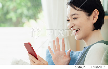 リビングでスマートフォンを操作する主婦 リビングでスマートフォンを操作する主婦 114082093