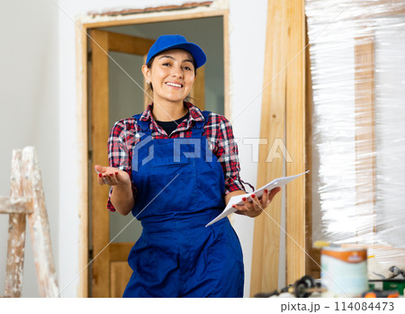 Positive woman builder with documents in apartment 114084473