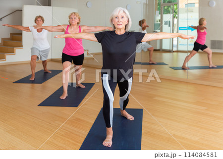 Three mature women perform the exercise by taking the warrior pose II 114084581