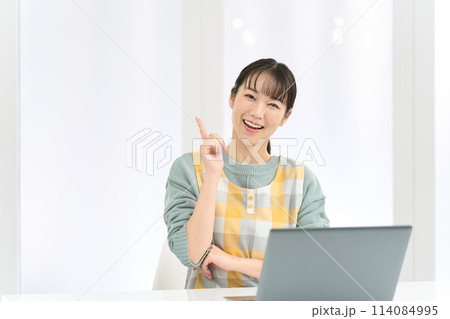 パソコン作業で良いことを思いつくエプロンを着た女性 114084995
