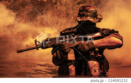 A bearded soldier performs a surveillance task in the water, walking through a swamp, surrounded by mist fog, rifle at the ready for imminent threats, colorized toned shot A bearded soldier performs a surveillance task in the water, walking through a swamp, surrounded by mist fog, rifle at the ready for imminent threats, colorized toned shot 114091232