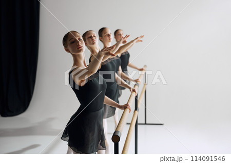 Ballet practice at barre. Beautiful young girl, ballet dancers in black costumes training, preparing for performance against grey studio background Ballet practice at barre. Beautiful young girl, ballet dancers in black costumes training, preparing for performance against grey studio background 114091546