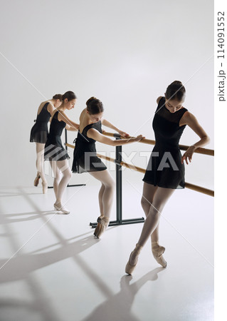 Discipline and focus. Tender teen girls, ballet dancers in black costumes attending dance class, training against grey studio background 114091552