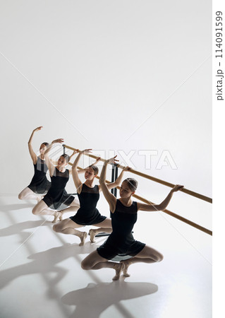 Elegance in training. Beautiful, focused teen girls, ballet dancers standing at barre and practicing against grey studio background Elegance in training. Beautiful, focused teen girls, ballet dancers standing at barre and practicing against grey studio background 114091599