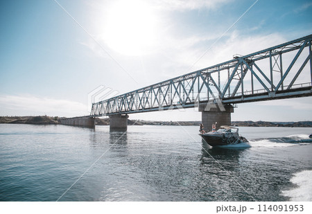 Boat floats on water under bridge on clear summer day Boat floats on water under bridge on clear summer day 114091953