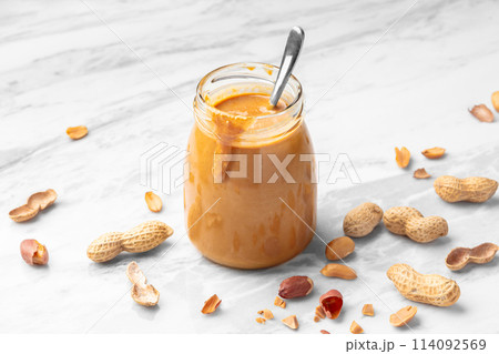 Peanut butter in glass jar on white marble table Peanut butter in glass jar on white marble table 114092569