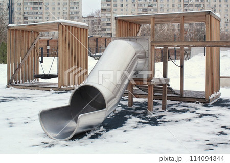 Wooden playground made of natural eco-friendly material in public city park with snow at winter time. Modern safety children outdoor equipment. Winter activities. Children rest and games on open air Wooden playground made of natural eco-friendly material in public city park with snow at winter time. Modern safety children outdoor equipment. Winter activities. Children rest and games on open air 114094844