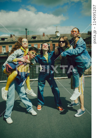 Joyful urban fashion vibe. Lively group of five friends enjoy sunny day on rooftop, wearing stylish denim clothes. Carefree, youthful spirit Joyful urban fashion vibe. Lively group of five friends enjoy sunny day on rooftop, wearing stylish denim clothes. Carefree, youthful spirit 114095207