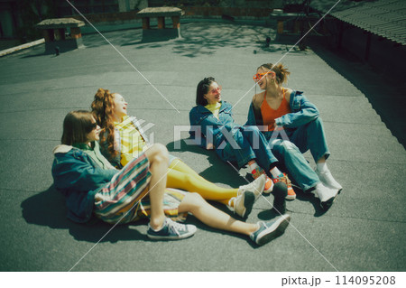 Group of friends spending time on city rooftop. Wearing trendy mix of streetwear, featuring denim and vibrant hues, reflecting their dynamic personalities. 114095208
