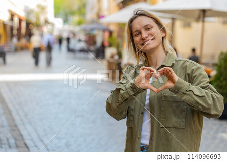 Woman makes symbol of love, showing heart sign to camera, express romantic feelings on city street Woman makes symbol of love, showing heart sign to camera, express romantic feelings on city street 114096693
