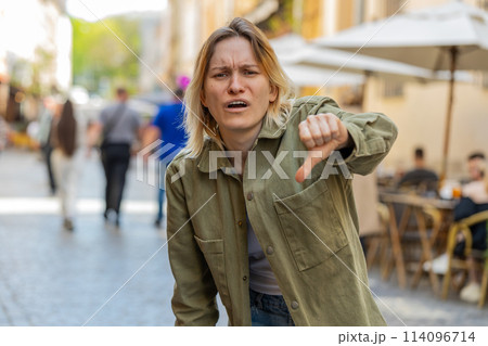 Upset young woman showing thumbs down sign disapproval, dissatisfied bad feedback on city street 114096714