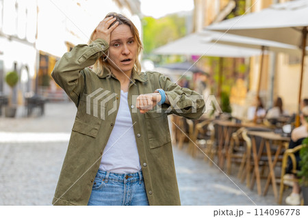 Scared young woman worrying to be punctual with anxiety checking time on watch running late to work 114096778