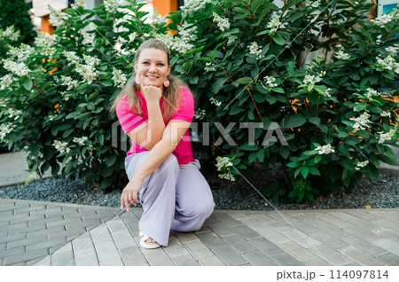 Portrait of beautiful smiling millennial woman wearing stylish pink t shirt looking at camera standing in green park. Positive lifestyle, natural beauty concept. Copy space Portrait of beautiful smiling millennial woman wearing stylish pink t shirt looking at camera standing in green park. Positive lifestyle, natural beauty concept. Copy space 114097814