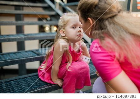 Deaf child with cochlear implant for hearing audio and aid for impairment having fun and laughs with mother outdoor in summer. Sound fitting device to help with communication listening and interaction 114097893