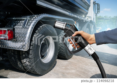 Hand with H2 nozzle on a background of hydrogen fuel cell truck. Eco-friendly commercial vehicle concept.. Hand with H2 nozzle on a background of hydrogen fuel cell truck. Eco-friendly commercial vehicle concept.. 114098218