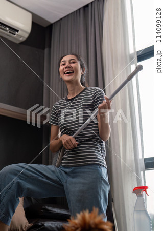 House cleaning with fun. Happy young asian housewife singing song during cleanup, using mop as guitar, enjoying domestic work. Young woman dancing and cleaning in living room House cleaning with fun. Happy young asian housewife singing song during cleanup, using mop as guitar, enjoying domestic work. Young woman dancing and cleaning in living room 114099128