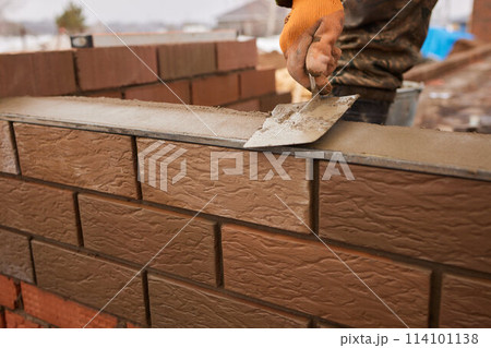professional construction worker laying bricks and building barbecue in industrial site. Detail of hand adjusting bricks 114101138