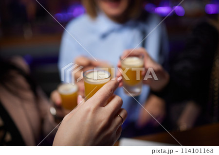 Group cheers with shot glasses of Paulaner hefeweizen wheat beer at fun event 114101168