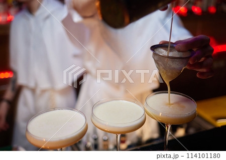 Bartender pours pink cocktail into martini glass with flair Bartender pours pink cocktail into martini glass with flair 114101180