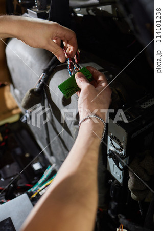 Auto electrician is connecting a wiring to car amplifier close up. Auto electrician is connecting a wiring to car amplifier close up. 114101238