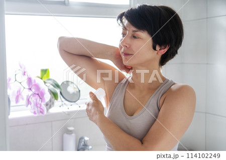 Young woman applying natural crystal alum deodorant in light modern bathroom. Eco friendly natural beauty and hygiene cosmetics. Zero waste, sustainable, alternative body care concept. Selective focus Young woman applying natural crystal alum deodorant in light modern bathroom. Eco friendly natural beauty and hygiene cosmetics. Zero waste, sustainable, alternative body care concept. Selective focus 114102249