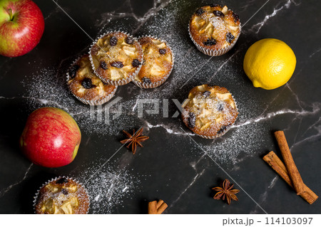 Homemade muffin with apples, raisins and cinnamon sticks. On a dark background Homemade muffin with apples, raisins and cinnamon sticks. On a dark background 114103097